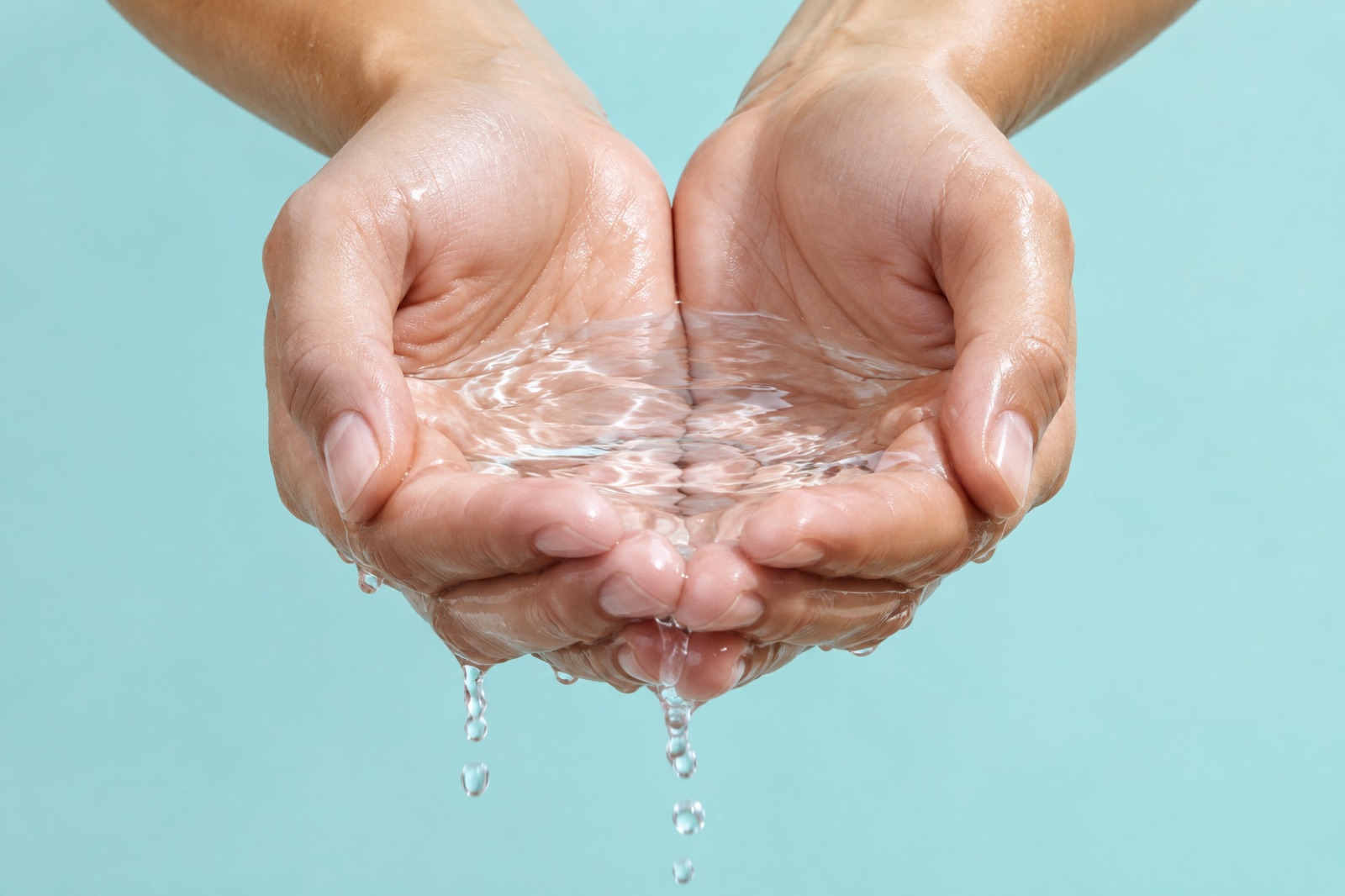 水色の背景の前で、すぼめた両手のひらに澄んだ水を受け、指の間から水の筋が落ちている様子