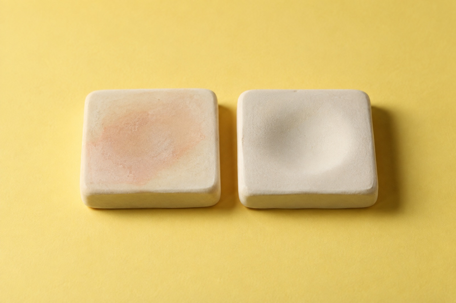 Two square clay tiles on a yellow background; the left one is stained pale pink in the center and the right one is pressed in