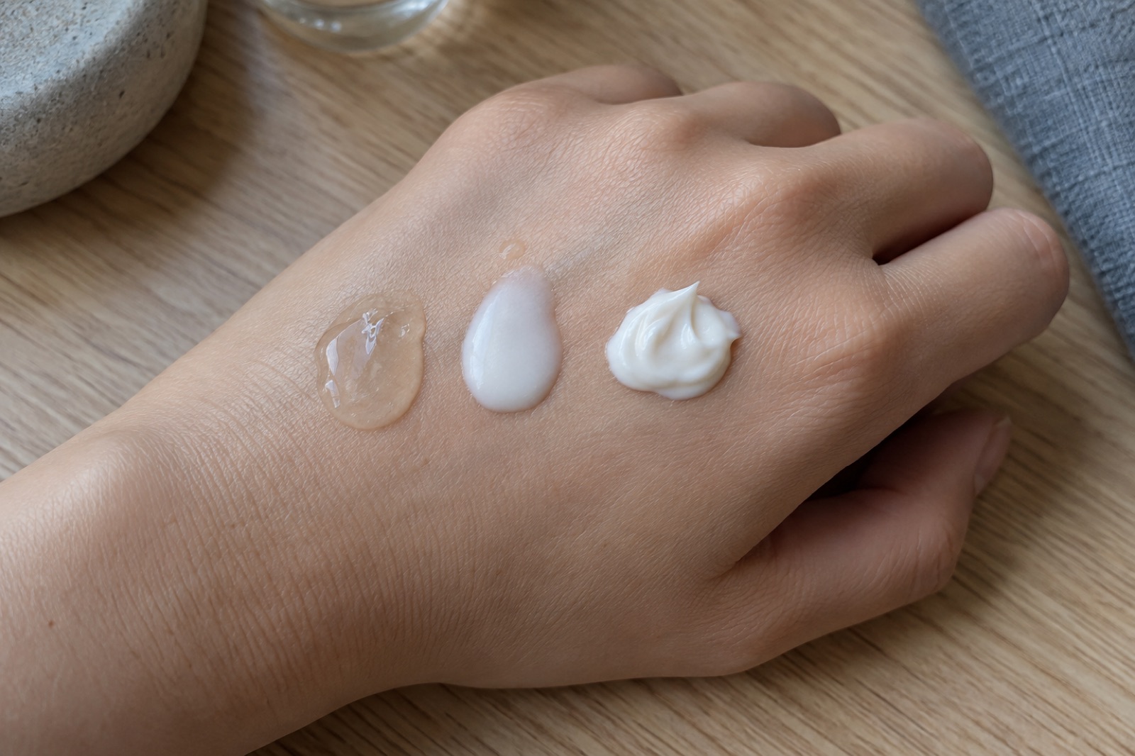 Clear gel, thin white lotion, and a peaked cream dabbed in a row on the back of a hand resting on a wooden table